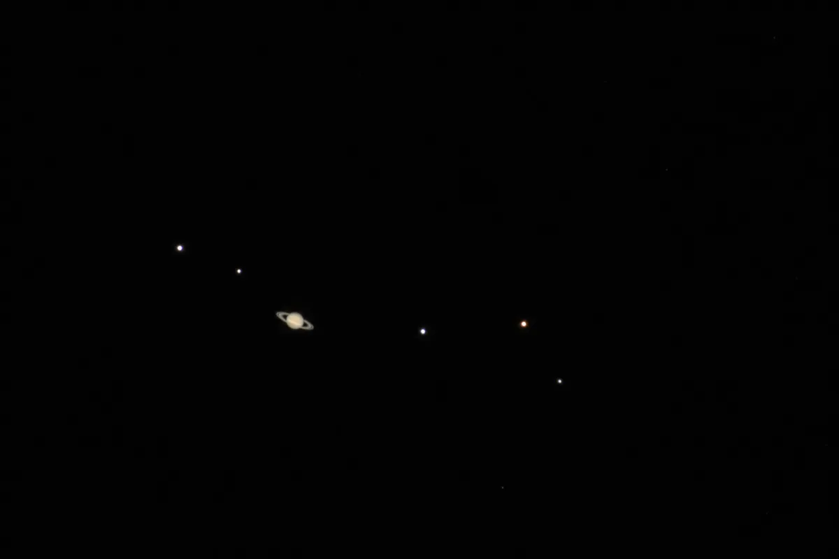 Champ télescopique montrant Saturne entourée de plusieurs points lumineux, ses satellites