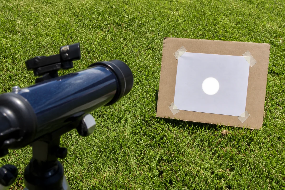 Feuille blanche recevant l&rsquo;image projetée du Soleil derrière l&rsquo;oculaire d&rsquo;une petite lunette, ombre nette sur l&rsquo;herbe
