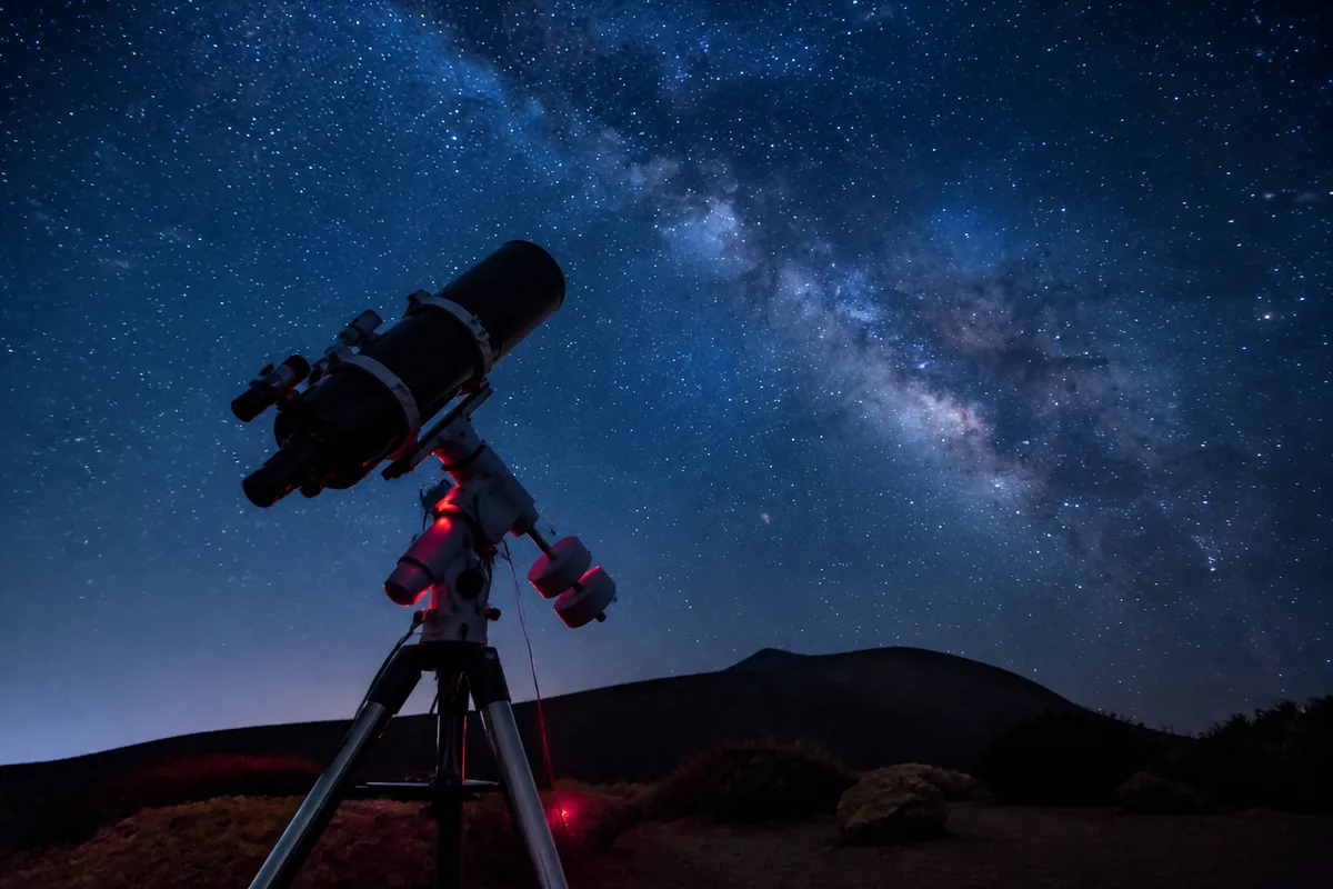 Télescope de type Dobson installé dans un jardin sombre, tube pointé vers un ciel étoilé dégagé
