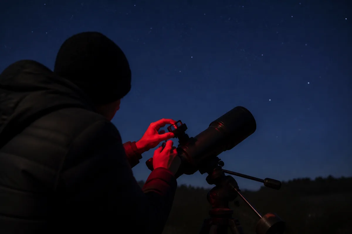 Débutant réglant le chercheur point rouge de son télescope sous un ciel étoilé