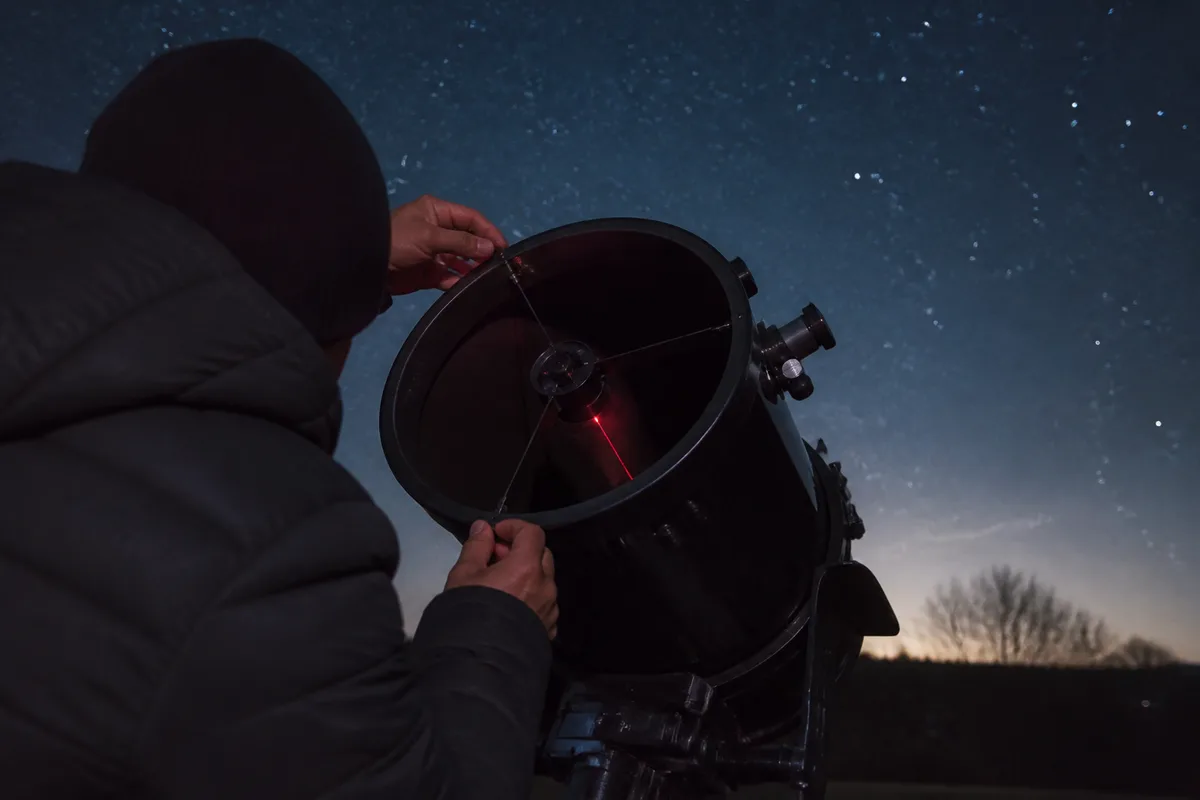 Observateur réglant la collimation d&rsquo;un télescope de Newton, faisceau laser rouge visible dans le tube